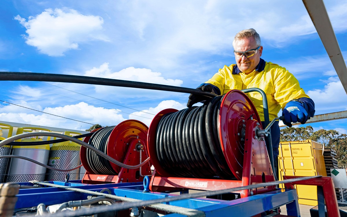 Man working with black hose on the back of a recovery truck 