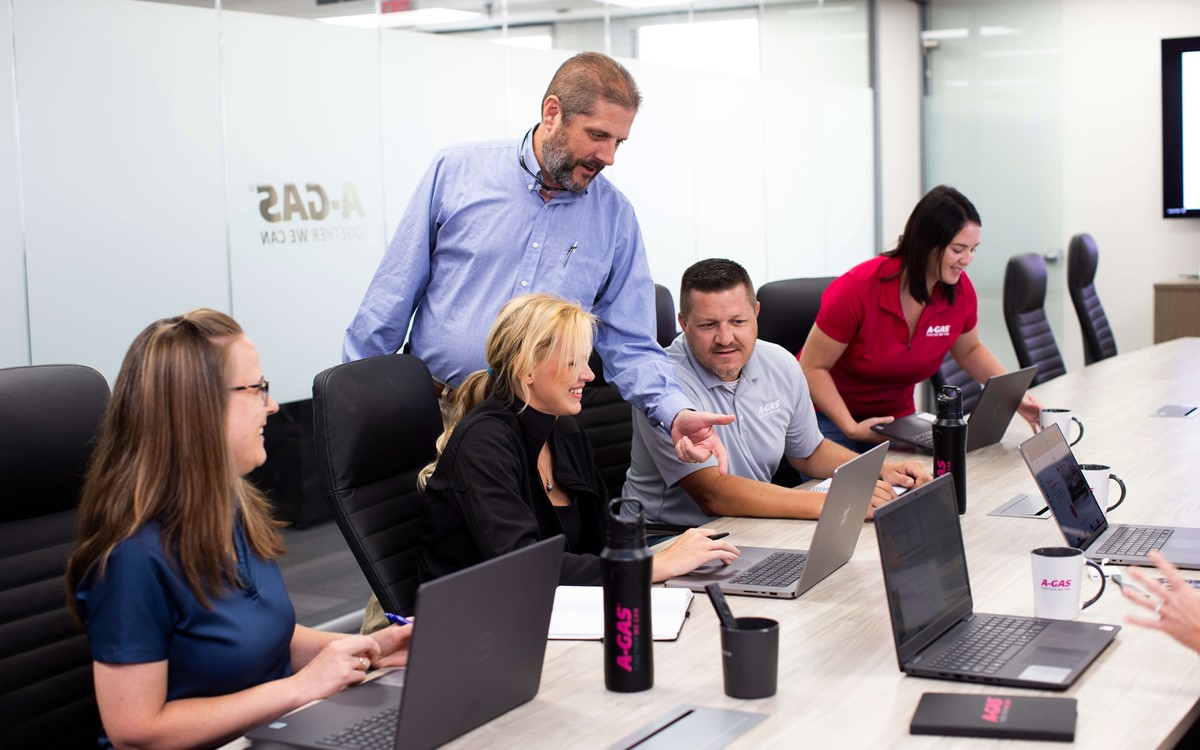 Men and women sat in the boardroom looking at a laptop, there is one man standing up pointing at the screen