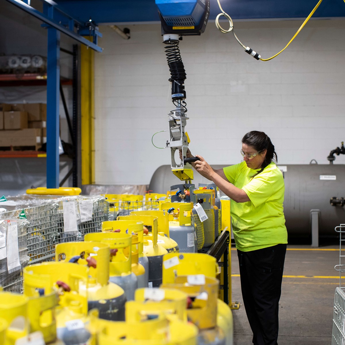 A woman in a warehouse operating a crane above metal baskets full of gas cylinders
