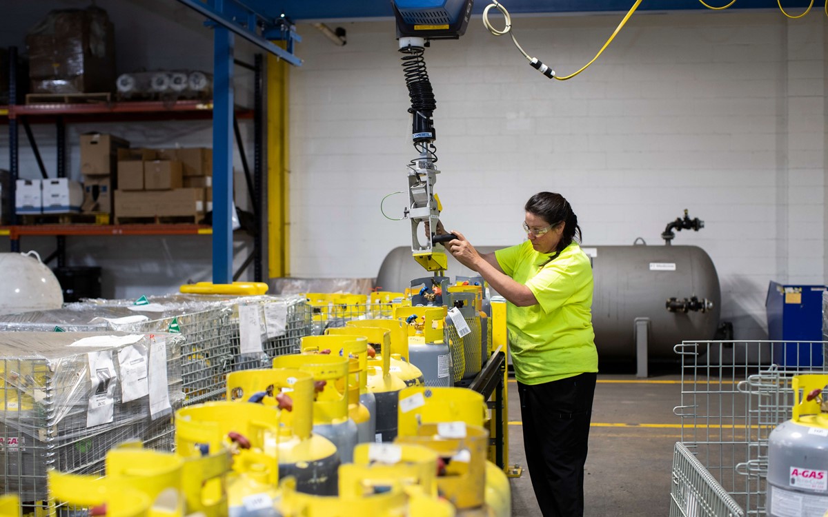 A woman in a warehouse operating a crane above metal baskets full of gas cylinders