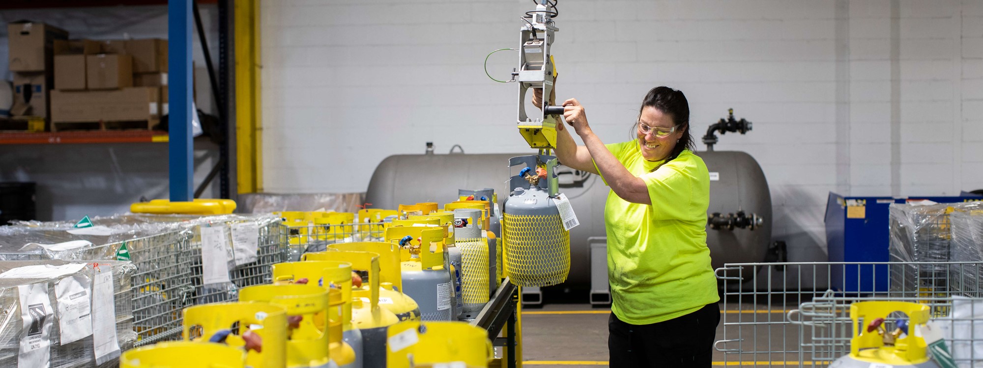 A woman in a warehouse operating a crane above metal baskets full of gas cylinders