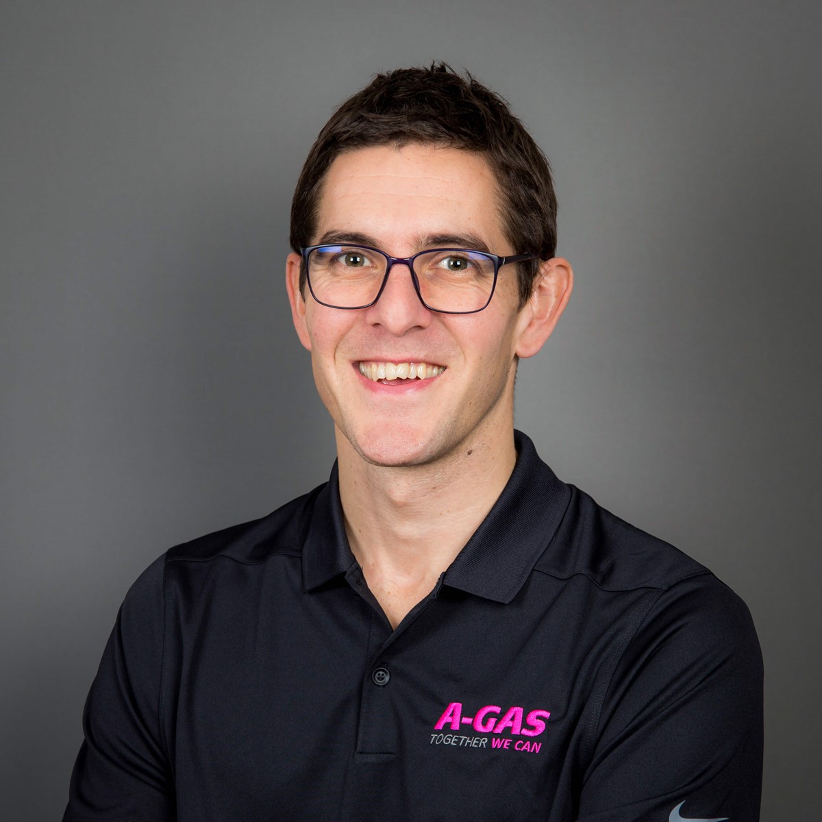 A headshot of a man in a black polo with a grey background 