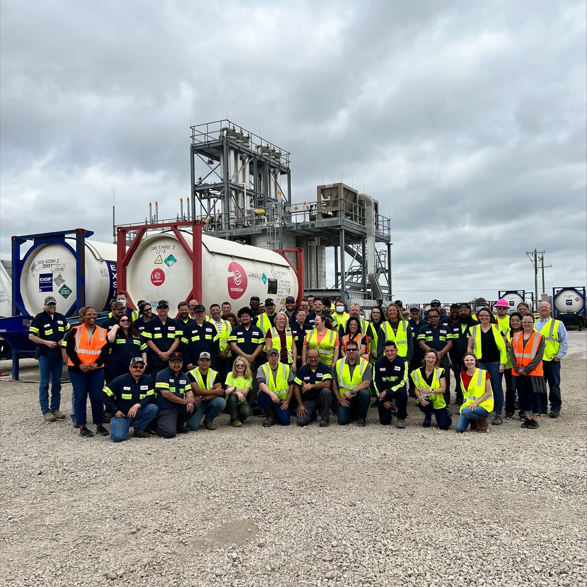 A team of warehouse workers outside lined up underneath industrial gas cylinders