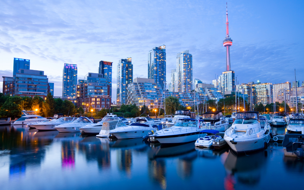 A city in Canada at night, there are boats parked on the water with the city lights of the buildings in the background reflecting in the water