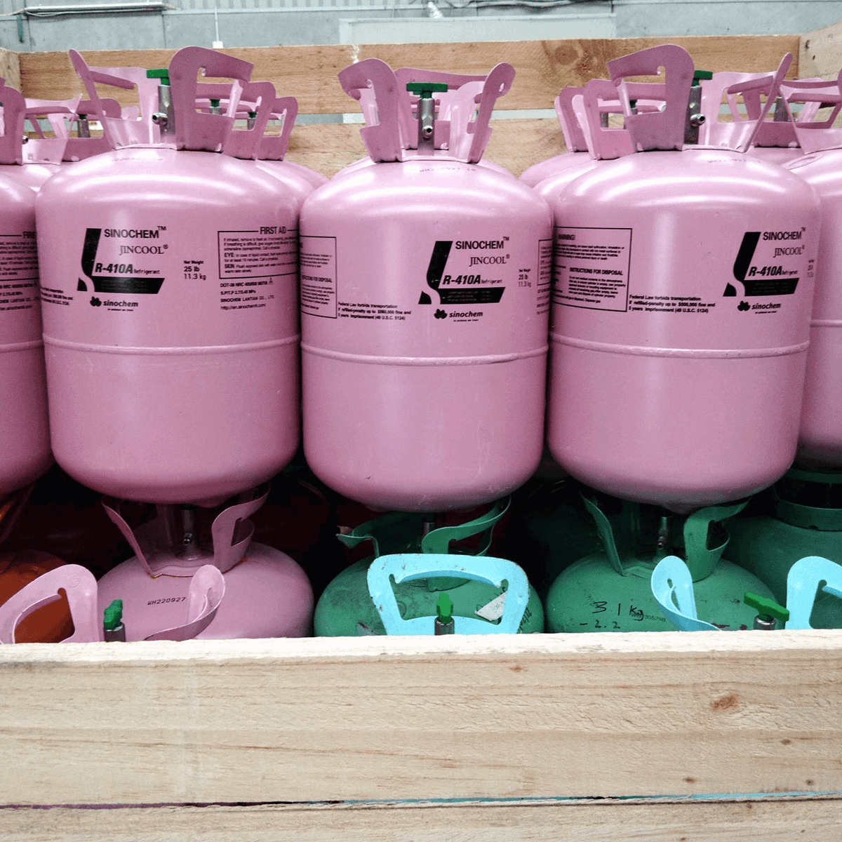 Rows of pink disposable cylinders on top of green, pink and red cylinders in a wooden crate 