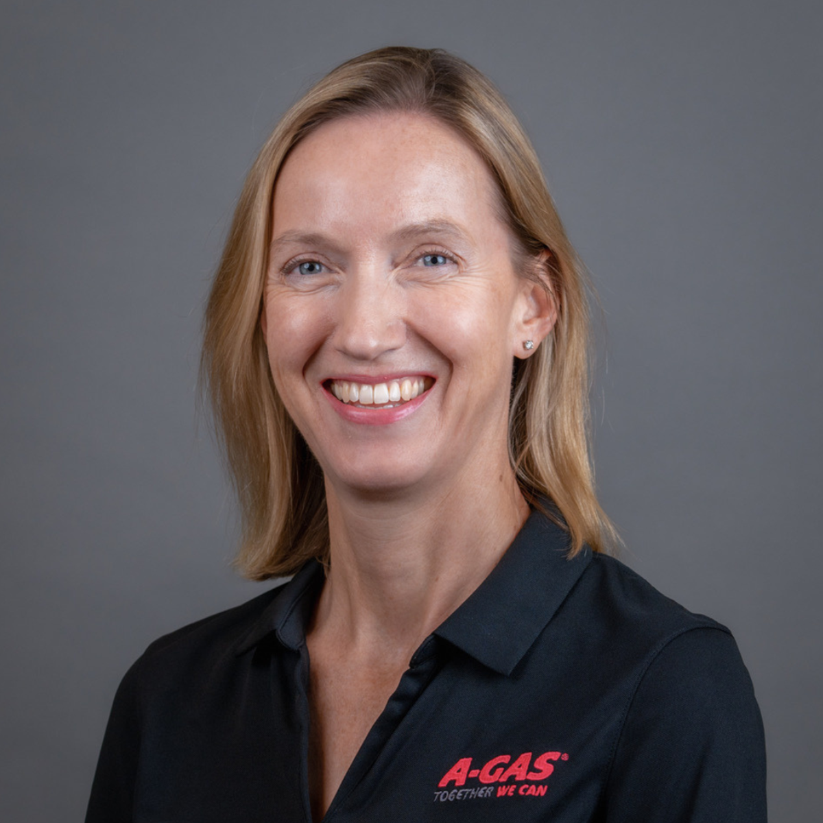 A headshot of a woman in a blue polo smiling with a grey background 